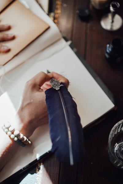 crop writer with feather and notepad at table in sunbeam